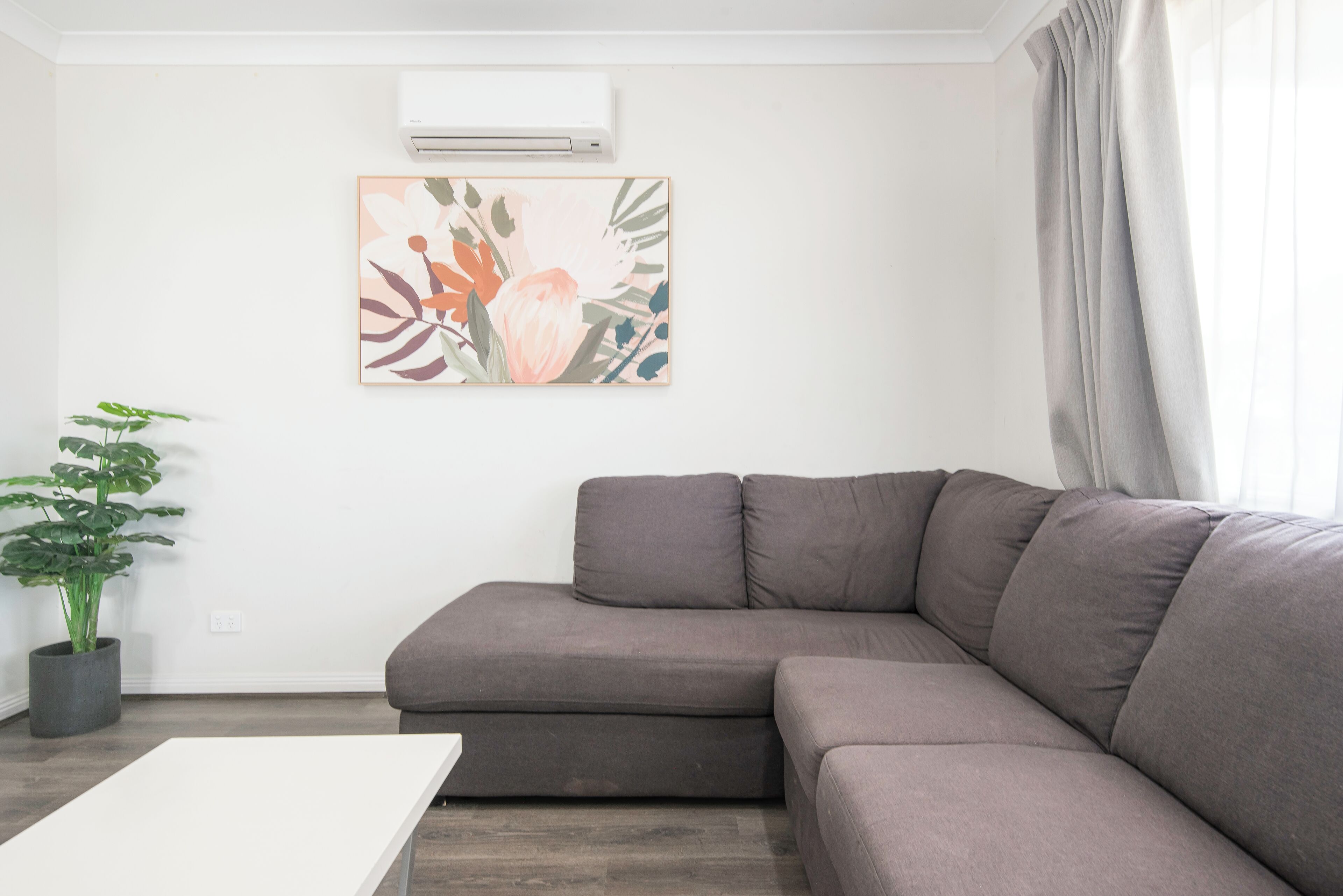 A modern living room with a gray sectional sofa, a white coffee table, a potted plant, and a floral artwork on the wall.