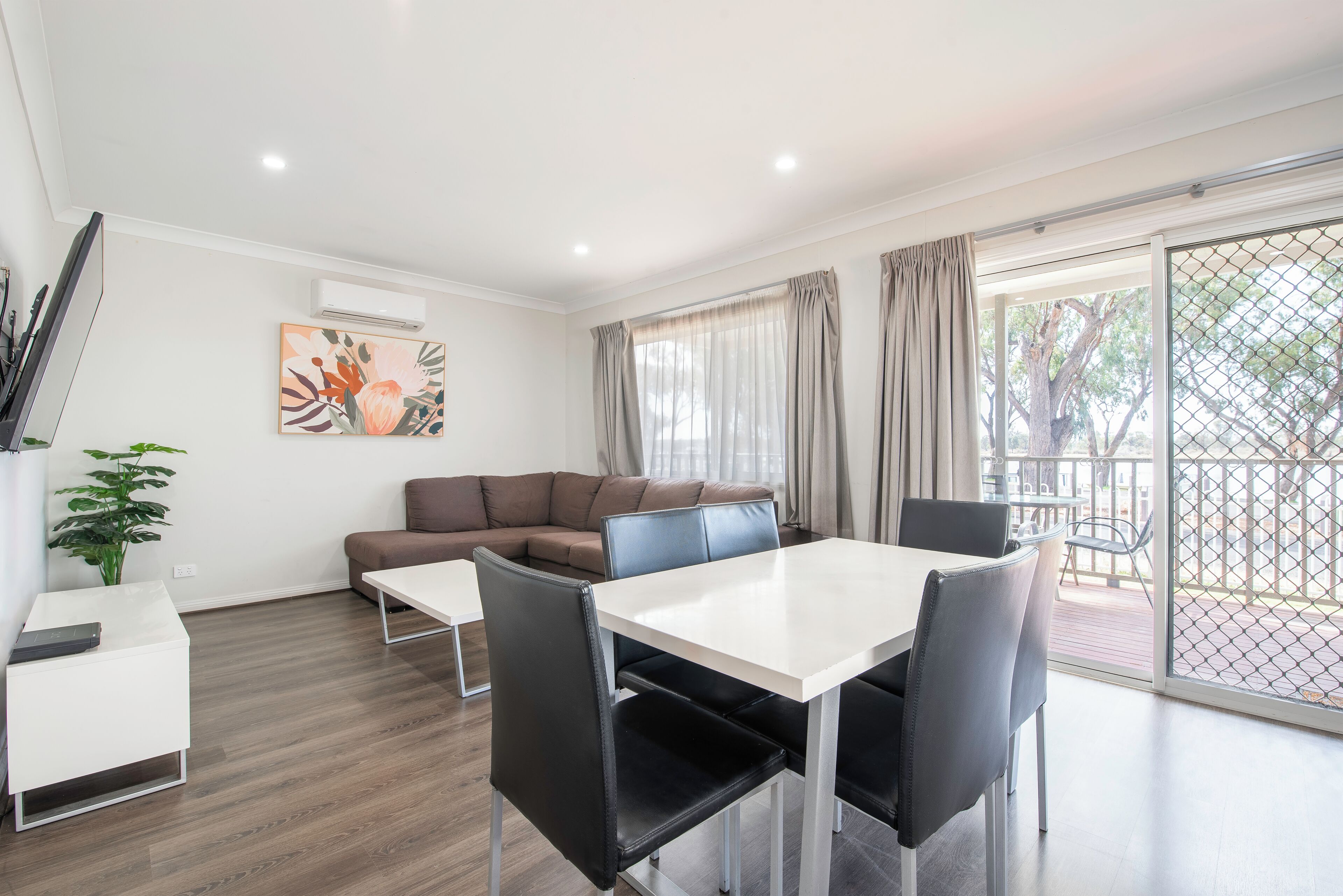 A modern living room with a sofa, a dining table with chairs, a potted plant, and a large window with curtains.
