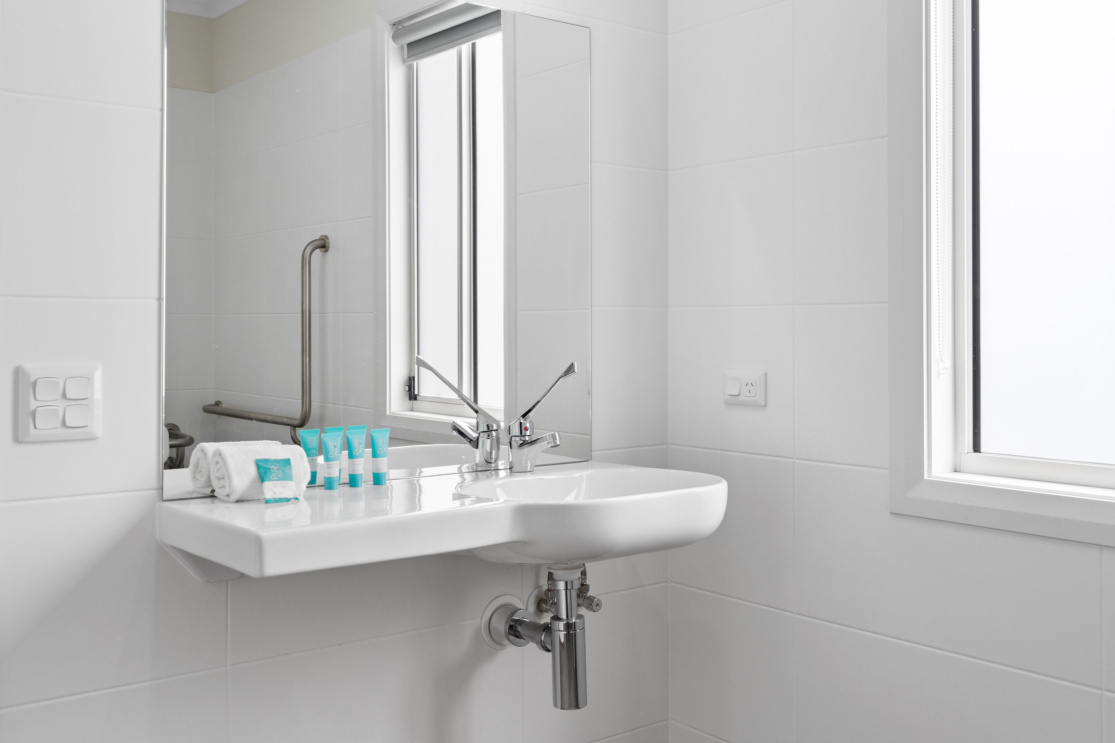 Un baño moderno con un lavabo blanco, espejo y toallero.