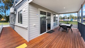 A covered outdoor area with a wooden deck, a table and chairs, and a sliding glass door leading to an interior space.
