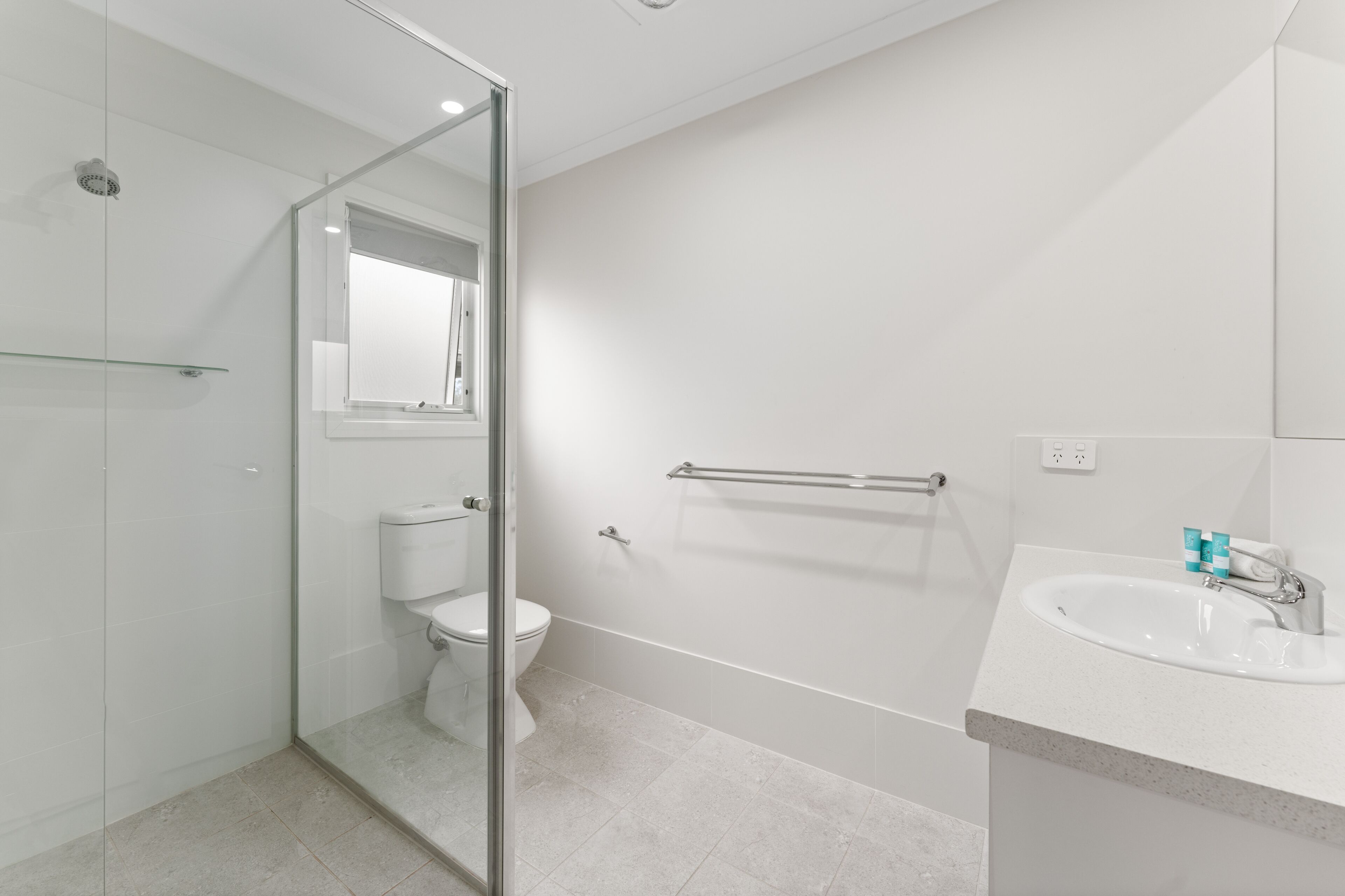 A modern bathroom with a glass shower enclosure, a white toilet, a glass shower door, a white sink with a mirror, and a towel rack.