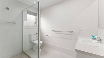 A modern bathroom with a glass shower enclosure, a white toilet, a glass shower door, a white sink with a mirror, and a towel rack.