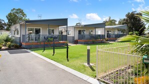 A row of two-story mobile homes with balconies, a paved driveway, and a fenced garden area.