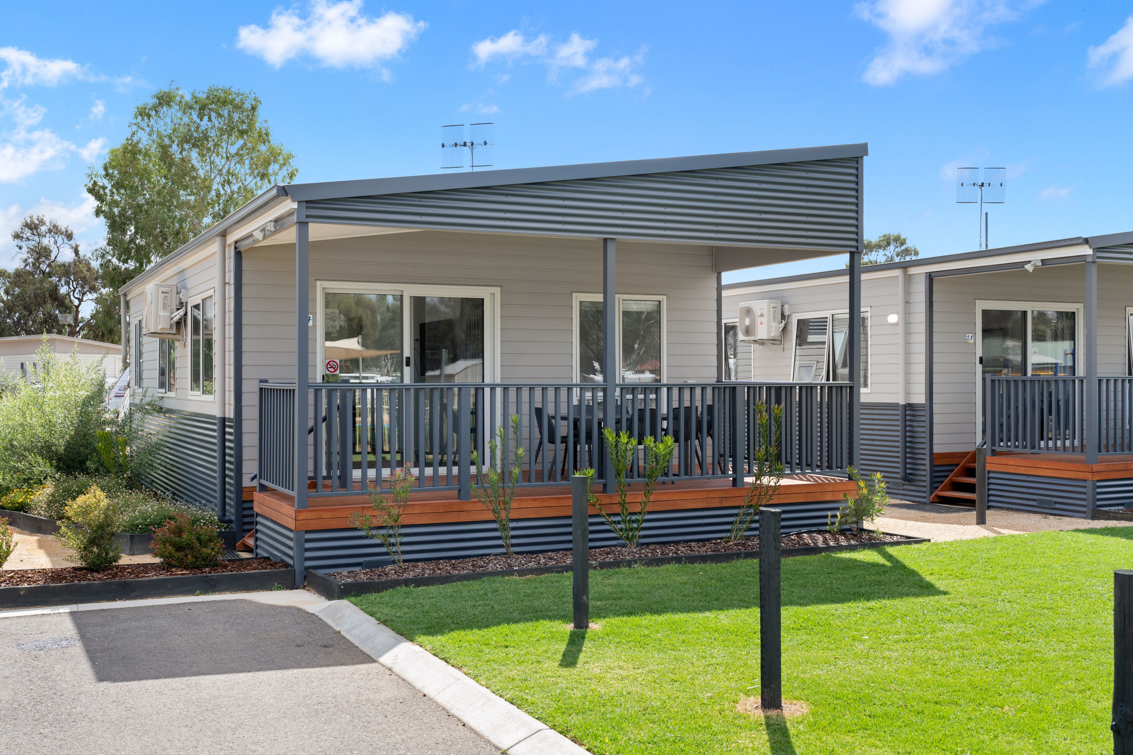 A modern mobile home with a covered porch, a small deck, and a well-maintained lawn.