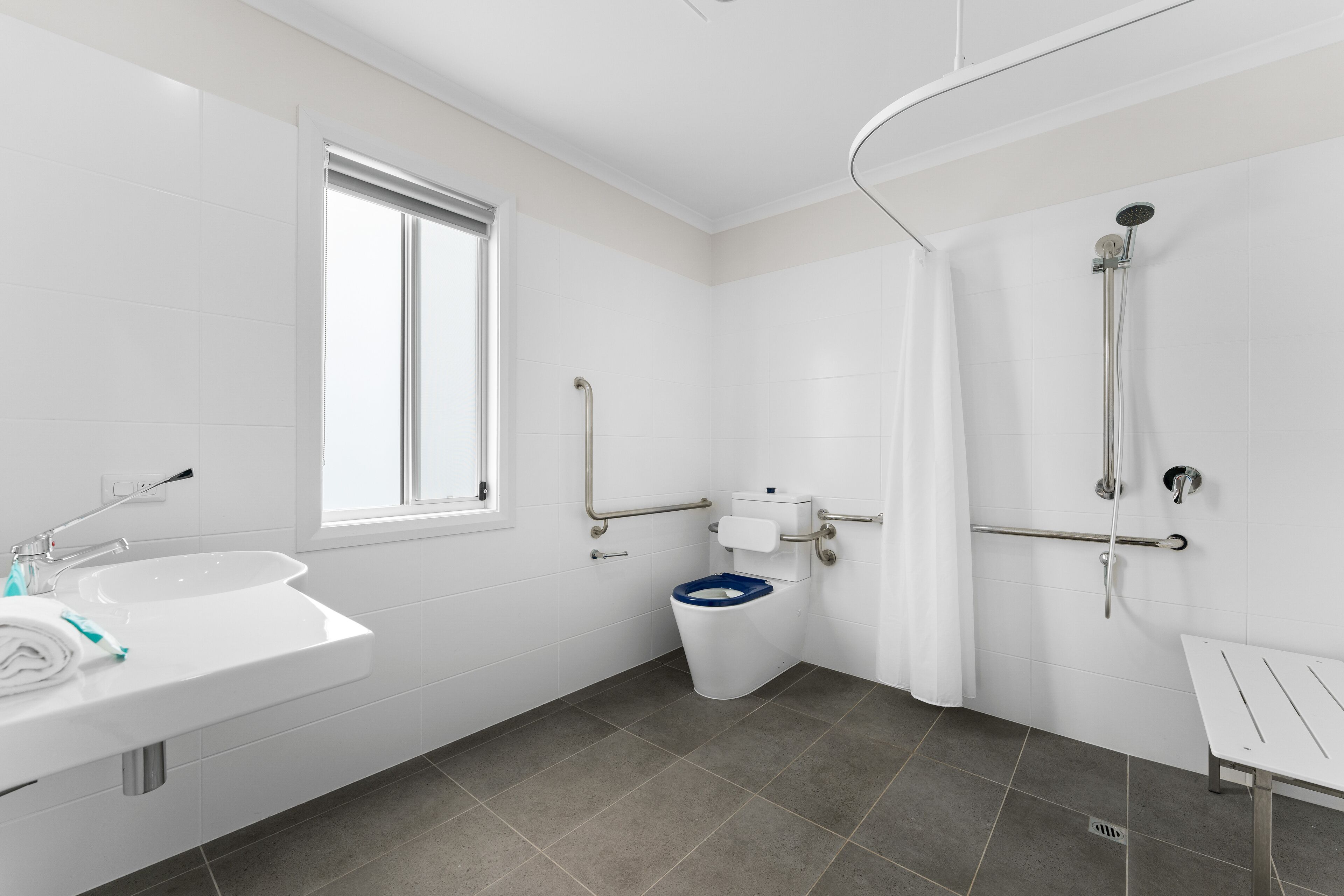 Een moderne badkamer met een witte wasbak, een toilet met een blauwe zitting en een douchegedeelte.