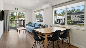 A modern room with a wooden table, black chairs, a blue sofa, and large windows offering a view of the outdoors.