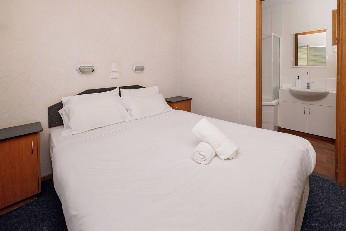 A hotel room with a bed, a nightstand, a bathroom with a sink and mirror, and a shower.