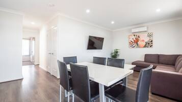 A modern living room with a dining table, black chairs, a brown sofa, and a potted plant.