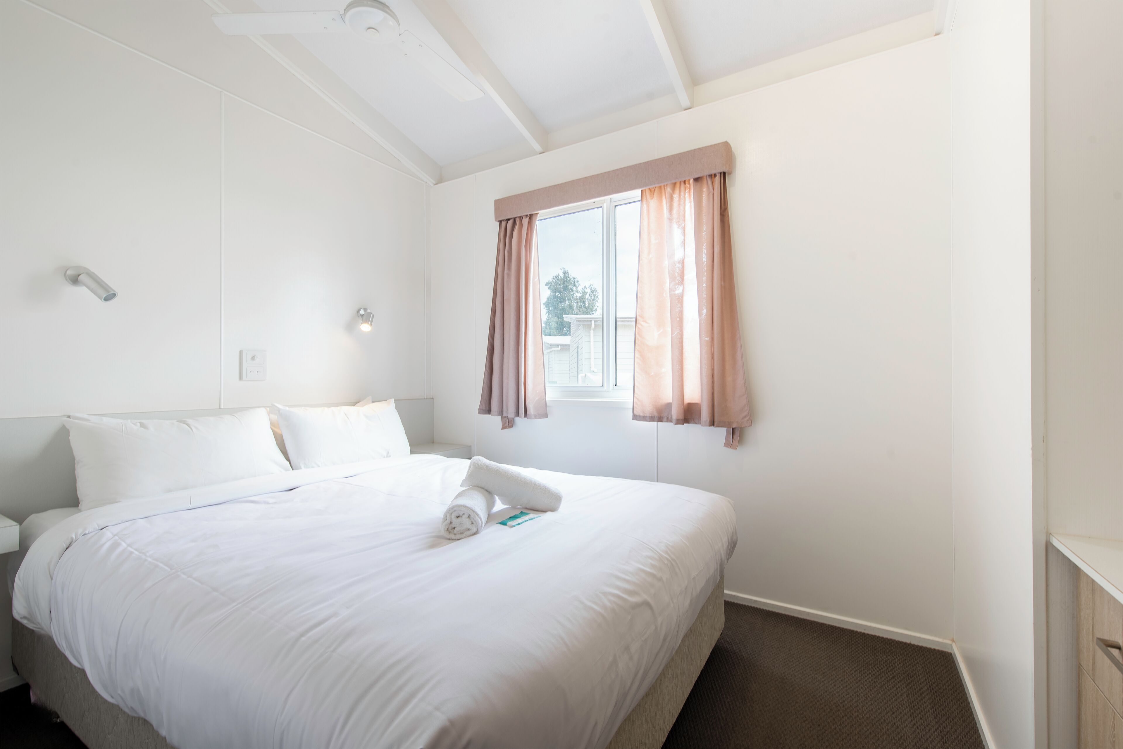 Habitación de hotel con una cama grande, una ventana con cortinas, una lámpara de techo y un enchufe de pared.