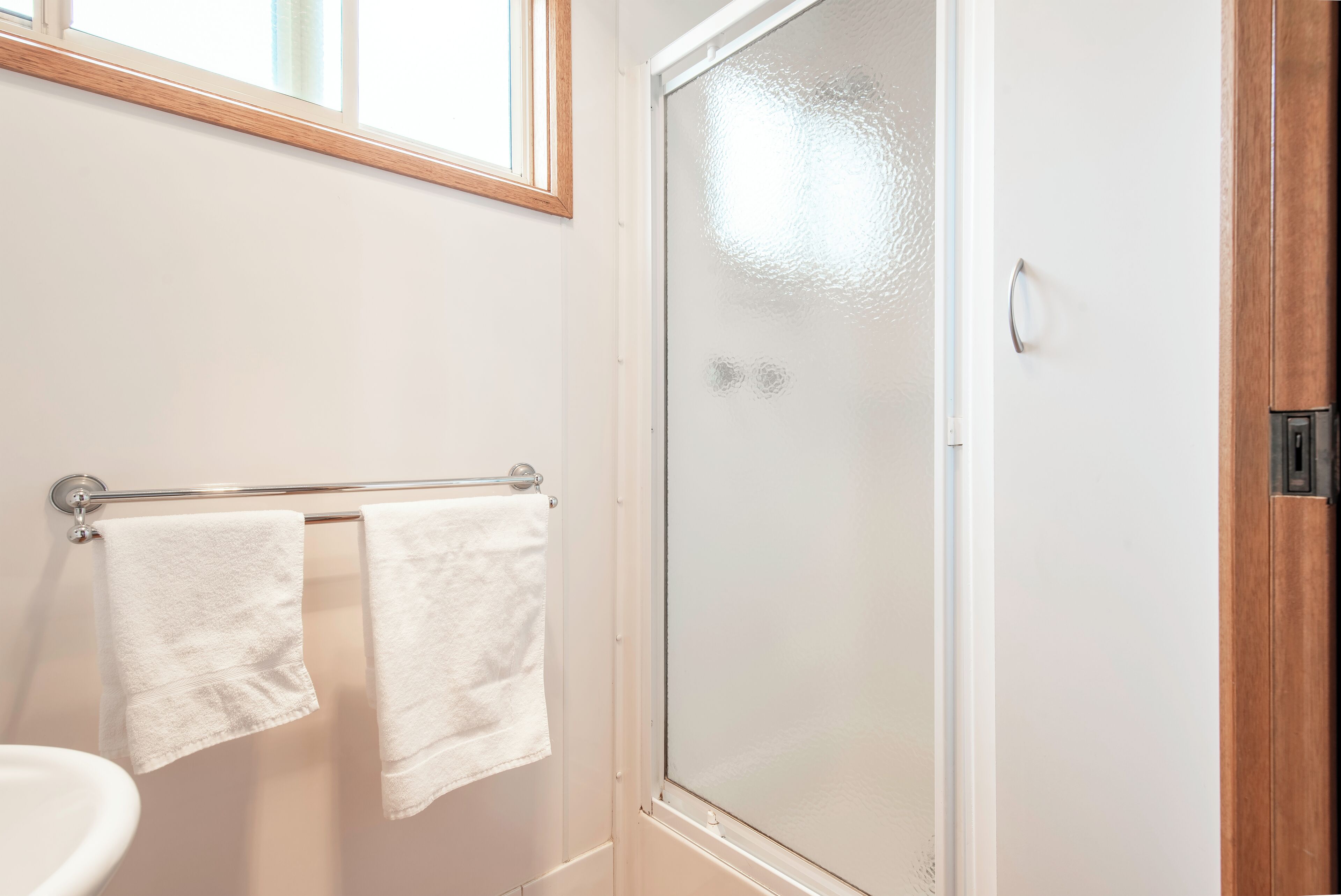 A bathroom with a glass shower door, a towel rack with two white towels, and a wooden cabinet.