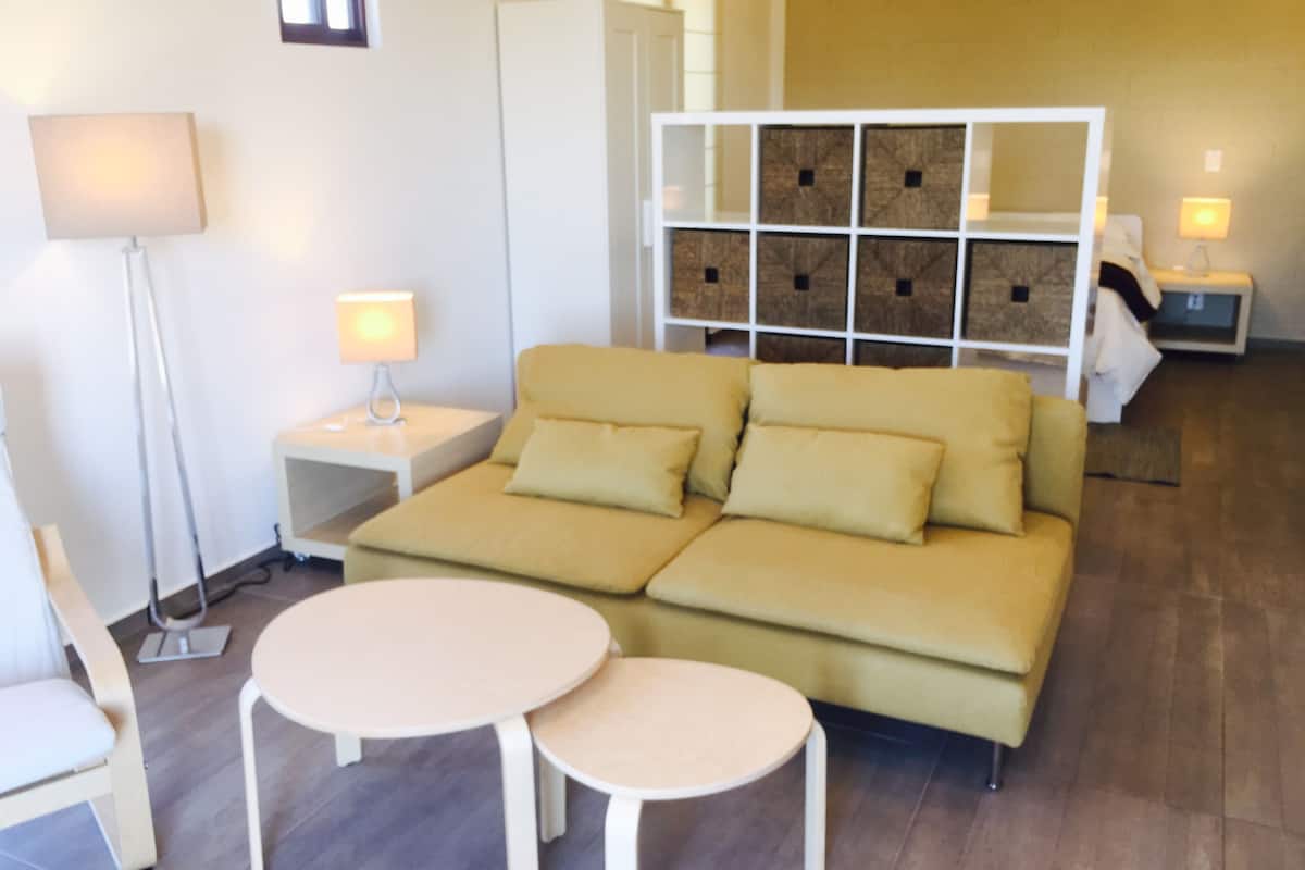 Una sala moderna con un sofá, dos mesas redondas, una lámpara de pie y un mueble de almacenaje con cajas.