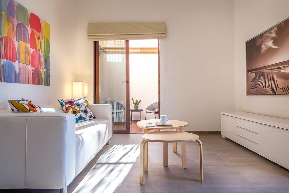 Una sala de estar moderna con un sofá blanco, una mesa redonda de madera y un cuadro abstracto grande en la pared.