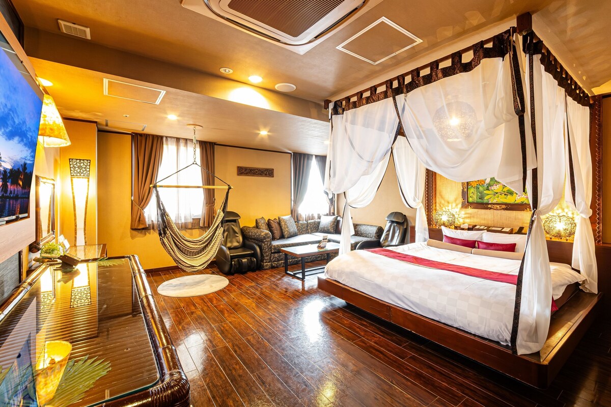 Een ruime slaapkamer met een groot bed, een zithoek met een bank en fauteuils, een hangstoel en een eettafel.