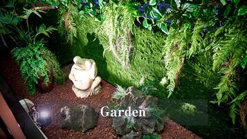 Un jardín con una estatua de rana, rocas y diversas plantas.