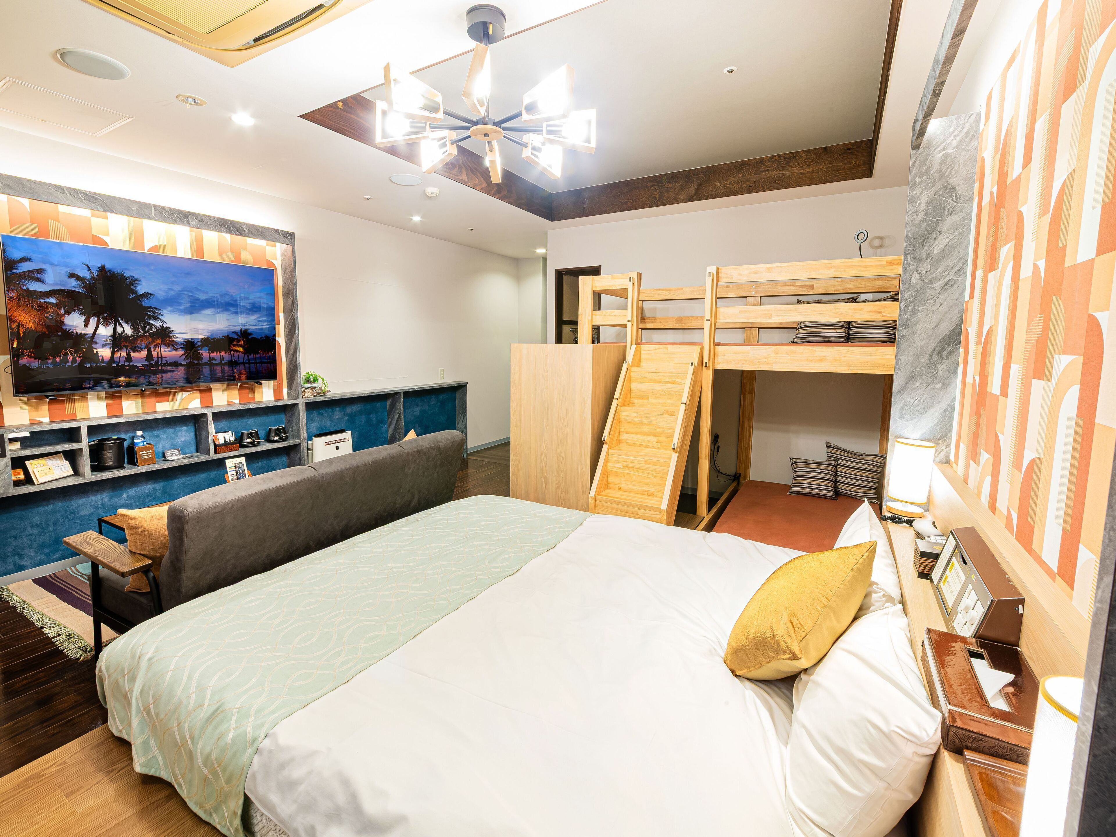A hotel room with a large bed, a bunk bed, a desk with a computer, a TV, and a painting of a beach scene.