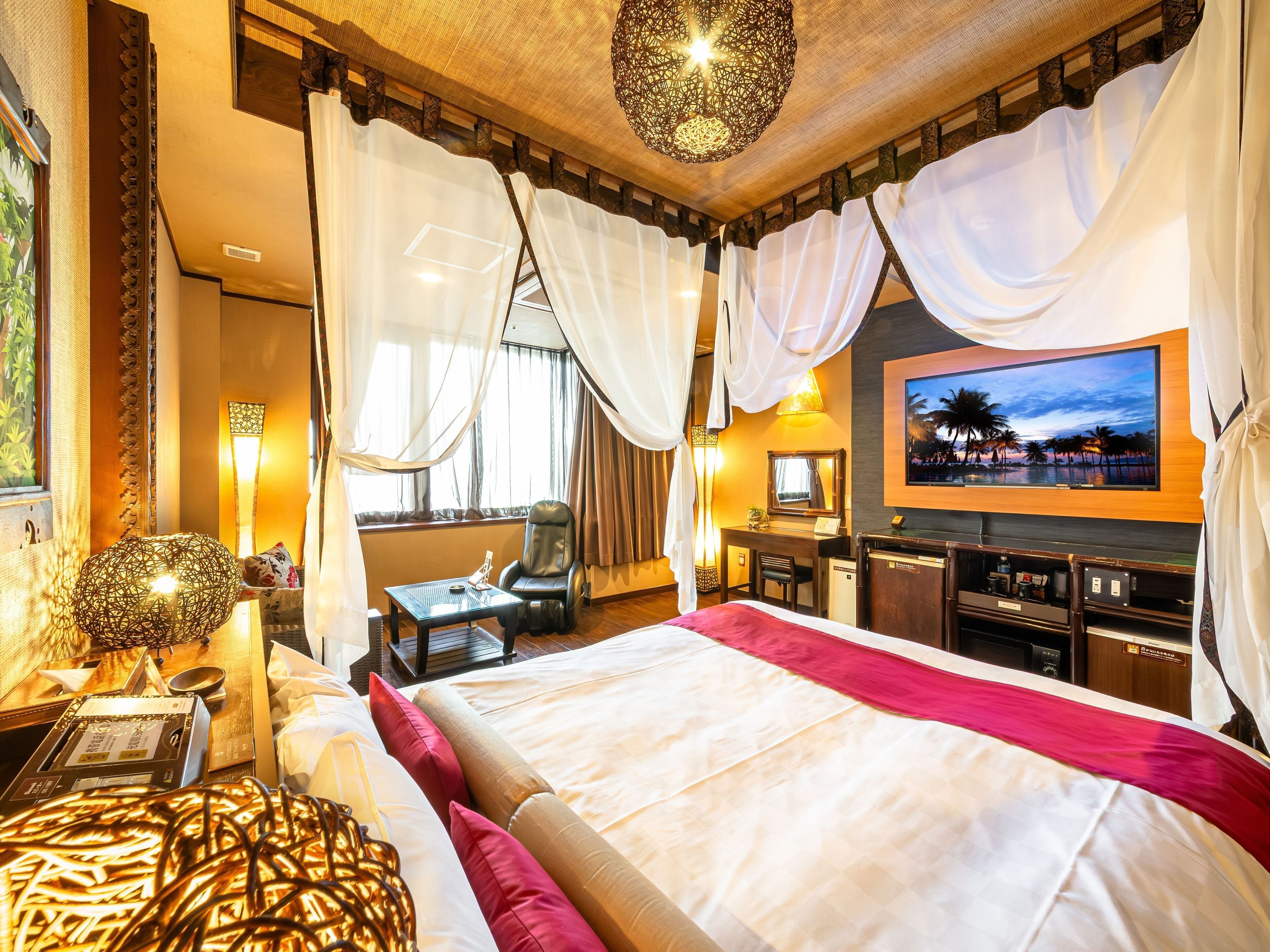 A hotel room with a large bed, a desk with a chair, a television, and a large window with curtains.