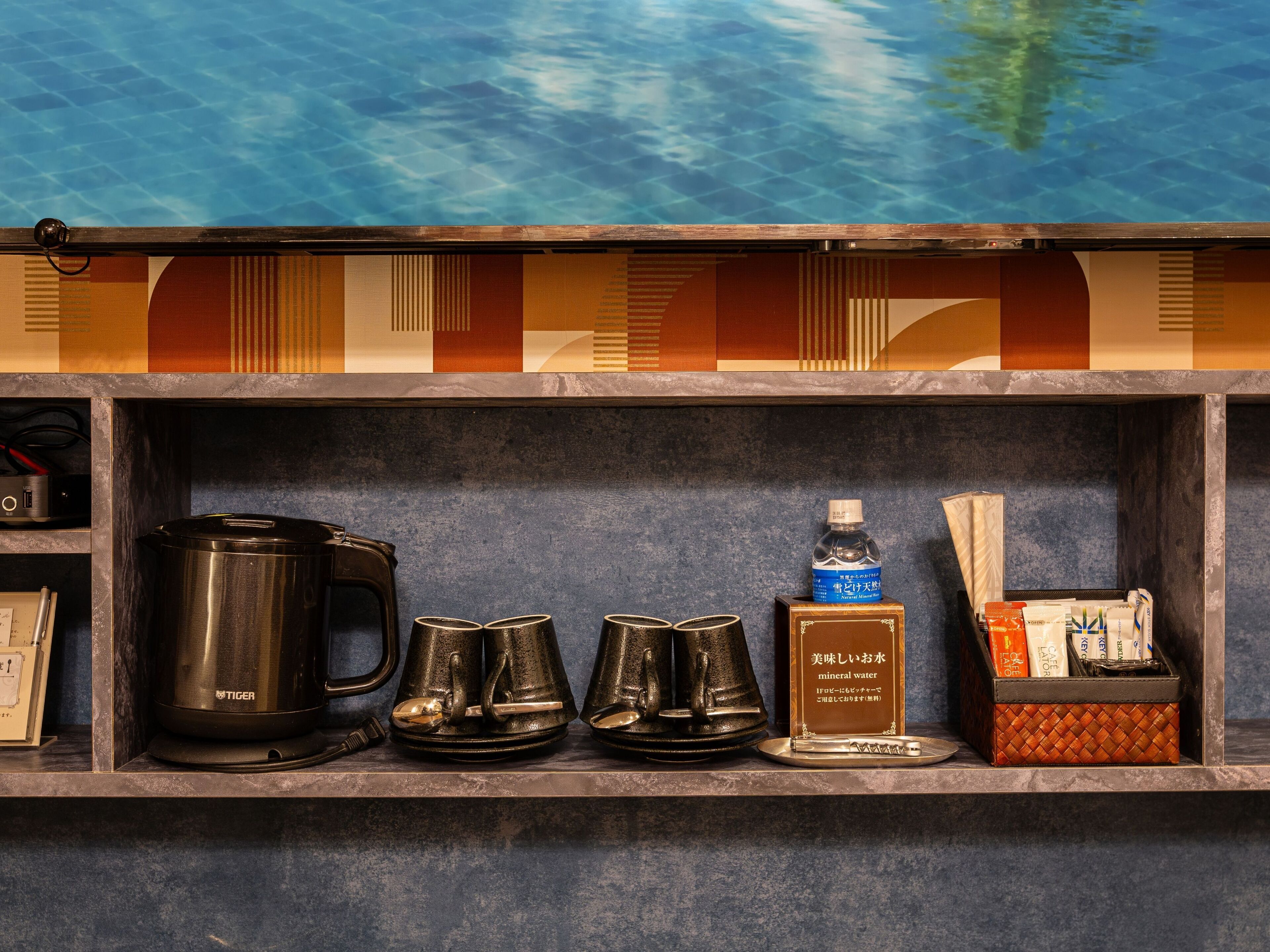 A shelf with a coffee maker, tea pots, a water bottle, and a box of coffee creamer.