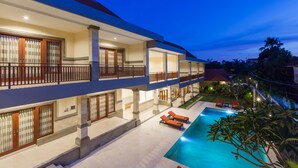A multi-story hotel with a swimming pool, outdoor seating, and a well-lit balcony area. - Kubu Petitenget Suite Seminyak (Keroboken Kelod)