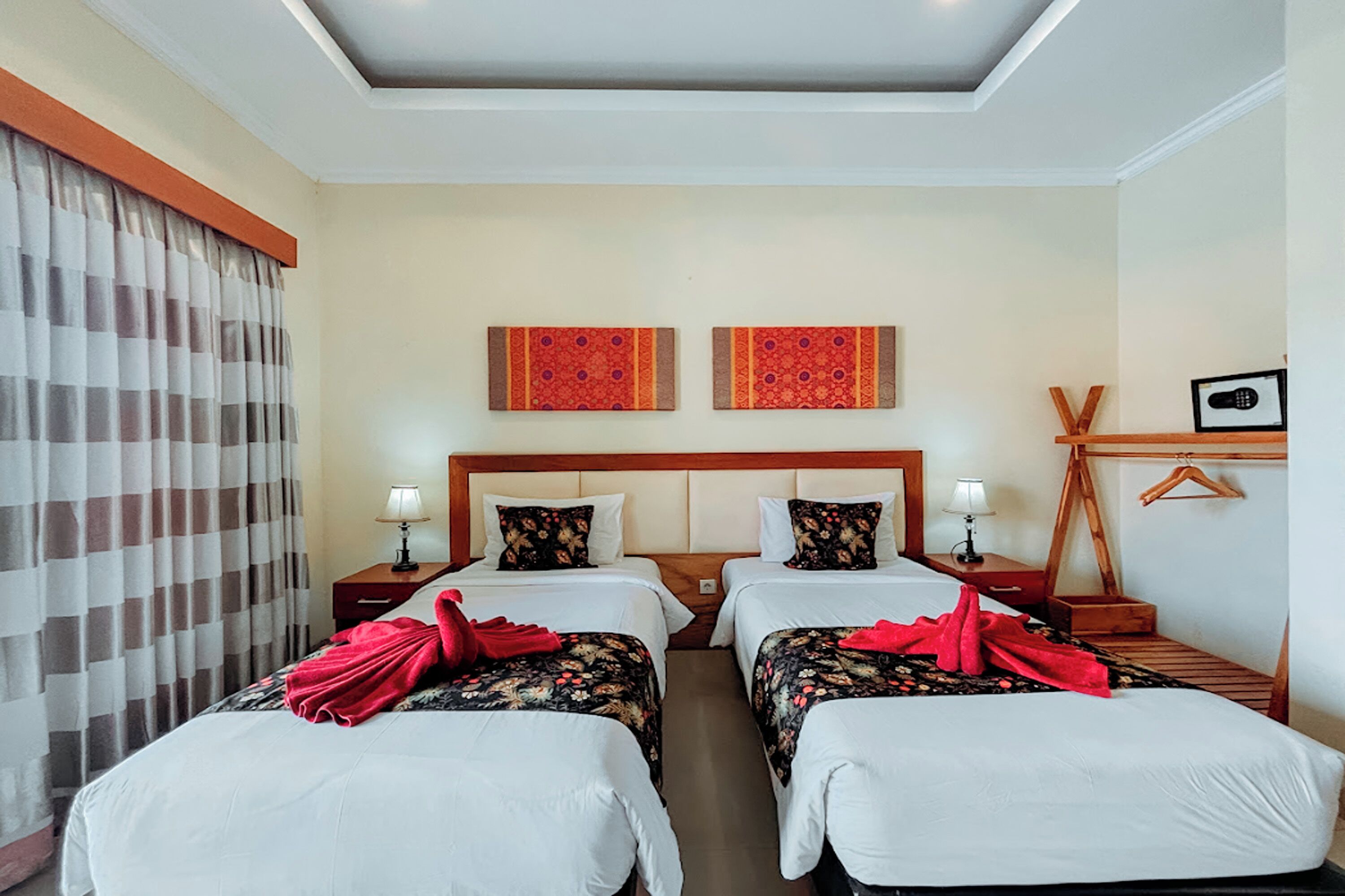 Une chambre d’hôtel avec deux lits, une tête de lit en bois, une table de chevet en bois avec une lampe, un porte-manteau en bois et un tableau encadré accroché au mur.