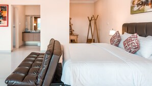 A modern bedroom with a large bed, a leather sofa, and a painting on the wall. - Kubu Petitenget Suite Seminyak (Keroboken Kelod)