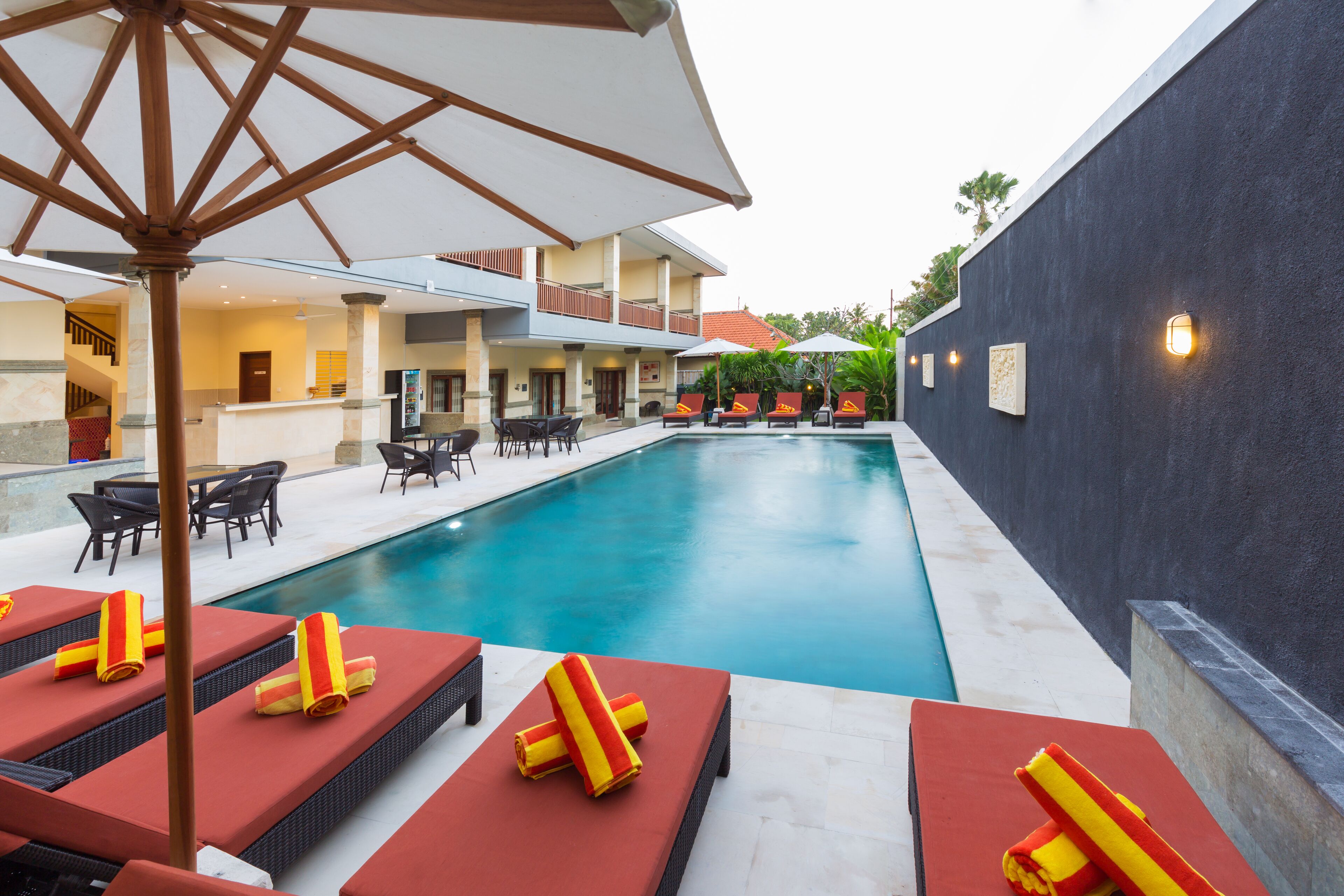 A swimming pool with lounge chairs and umbrellas, a bar area, and a building with balconies.