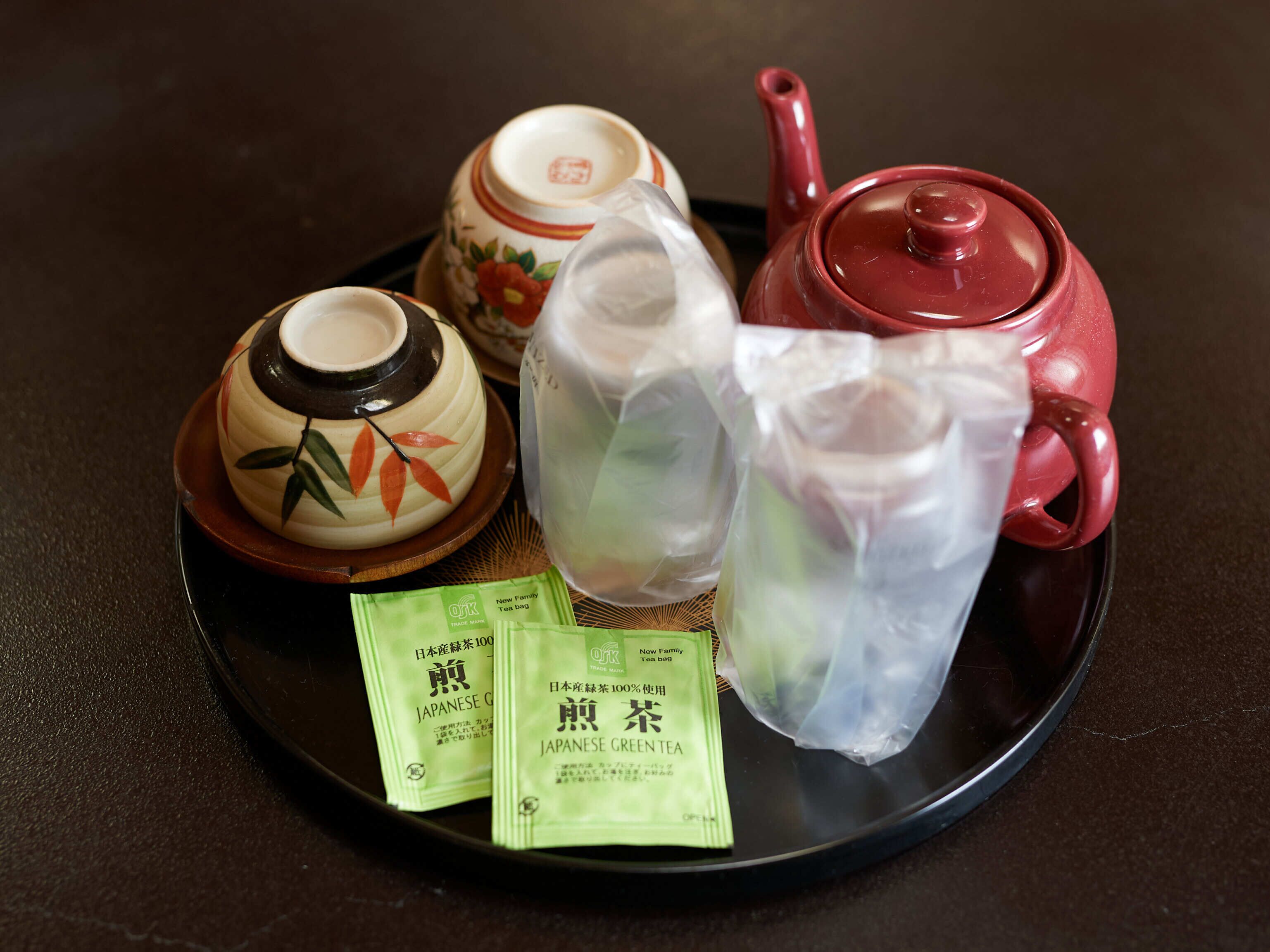 A traditional Japanese tea set on a tray, including a teapot, cups, and a small bowl, along with two packets of Japanese green tea.
