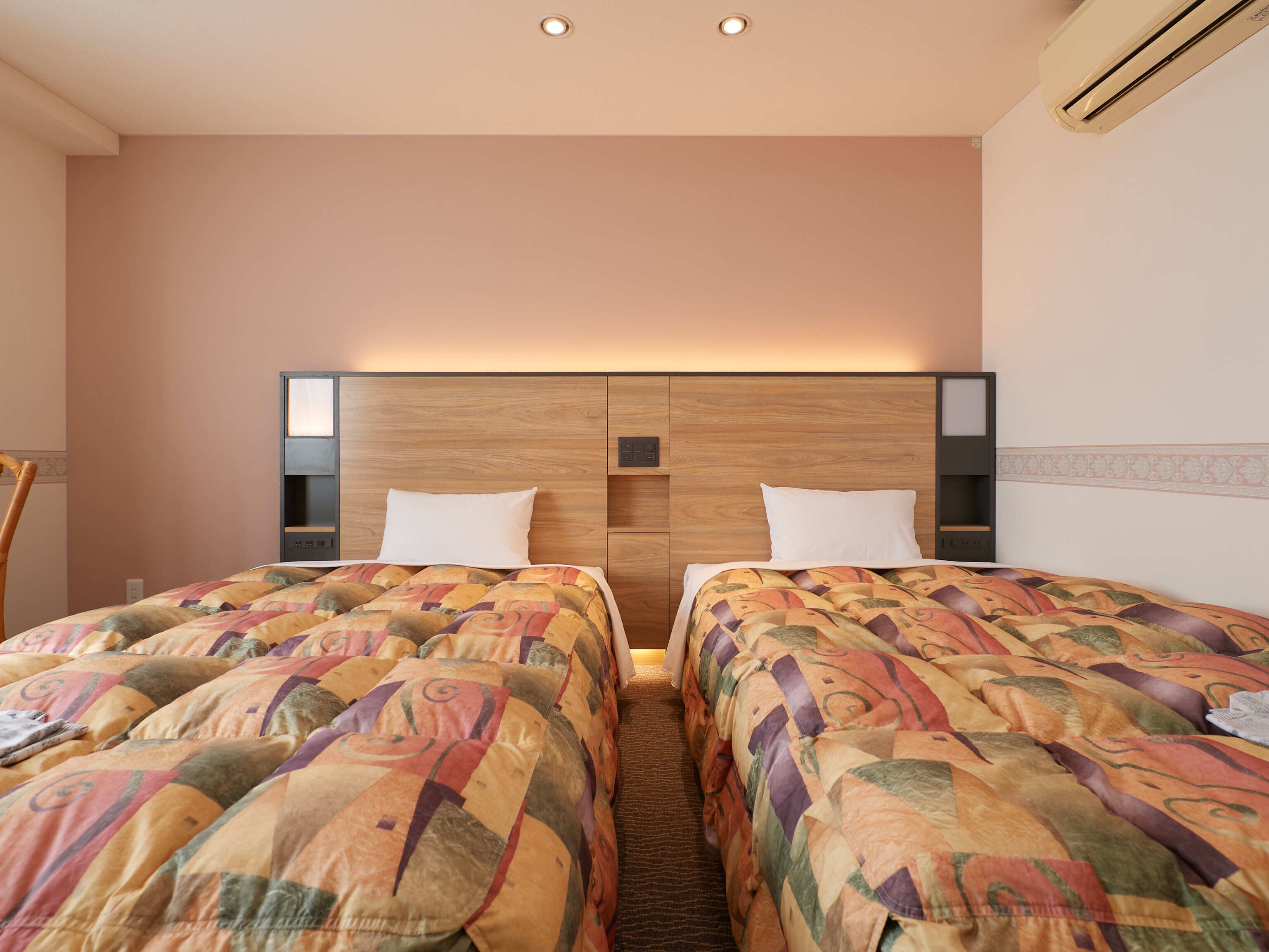 Habitación de hotel con dos camas, cabecero de madera y estante empotrado.