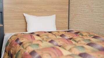 A neatly made bed with a patterned blanket and a white pillow against a wooden headboard.