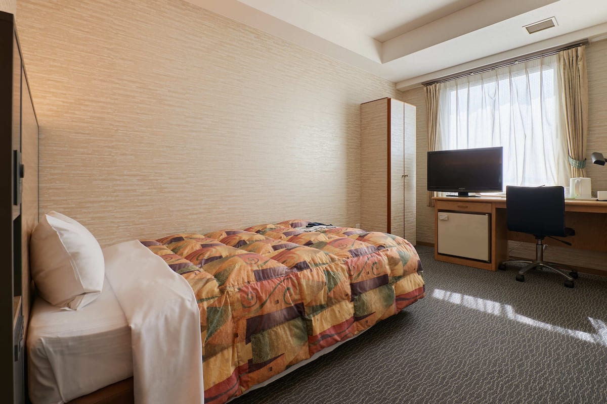 A hotel room with a bed, a desk with a computer, a TV, and a chair.