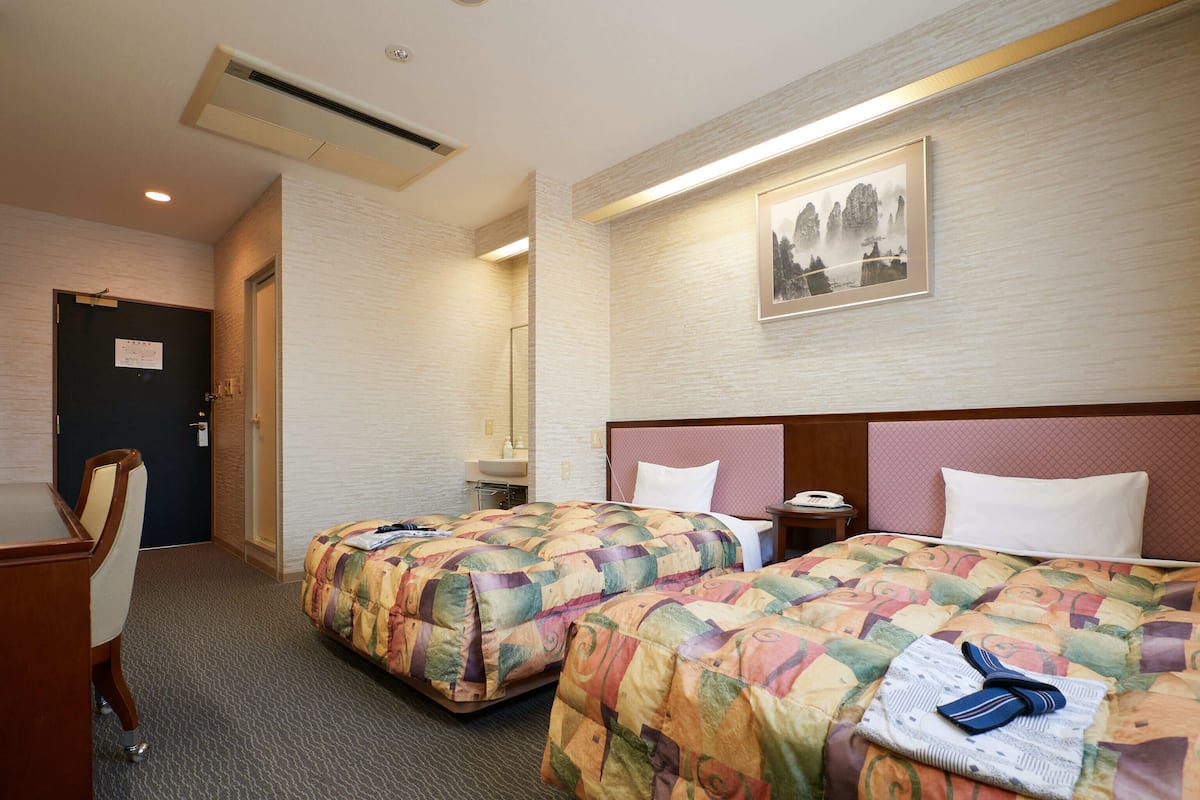 A hotel room with two beds, a desk, a chair, and a painting on the wall.