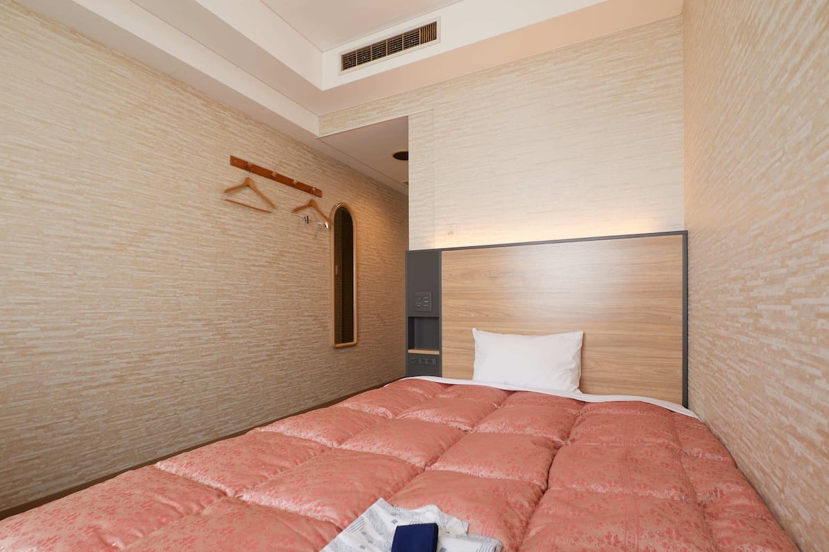A modern hotel room with a large bed, a wooden headboard, and a wall-mounted mirror.