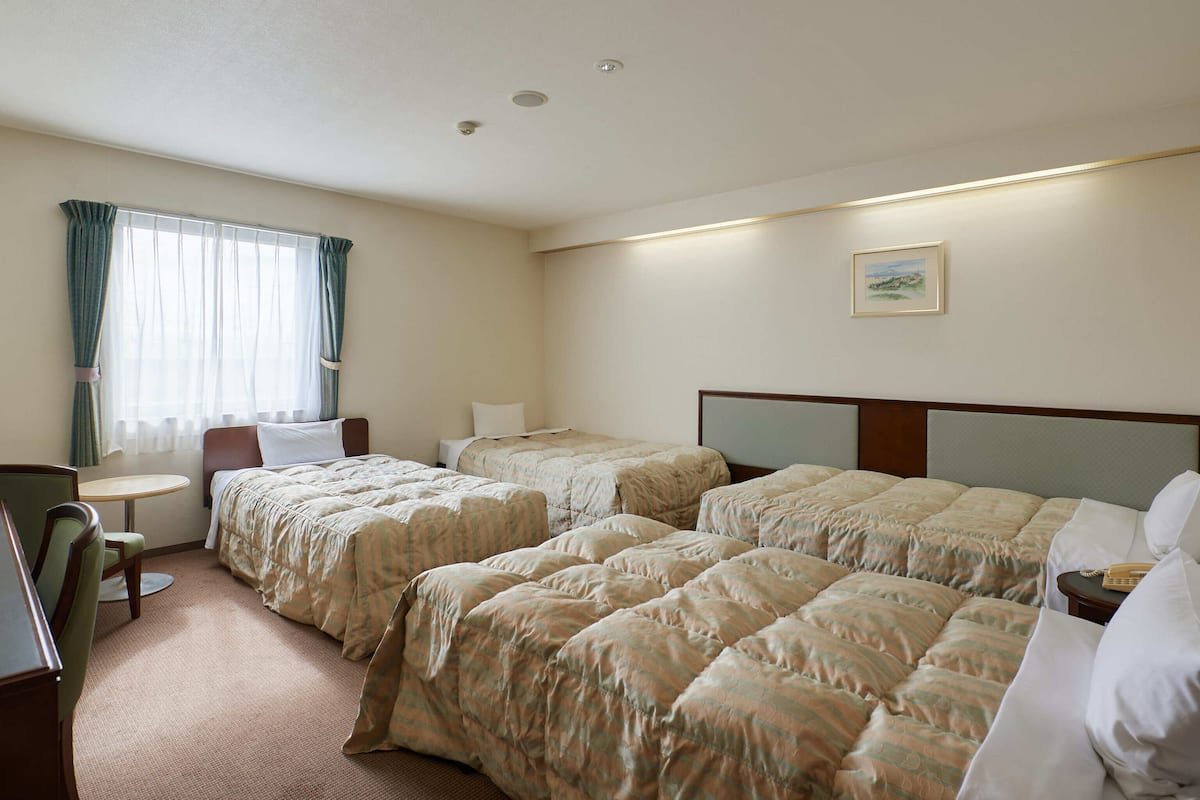 A hotel room with two beds, a desk, a chair, and a small table.