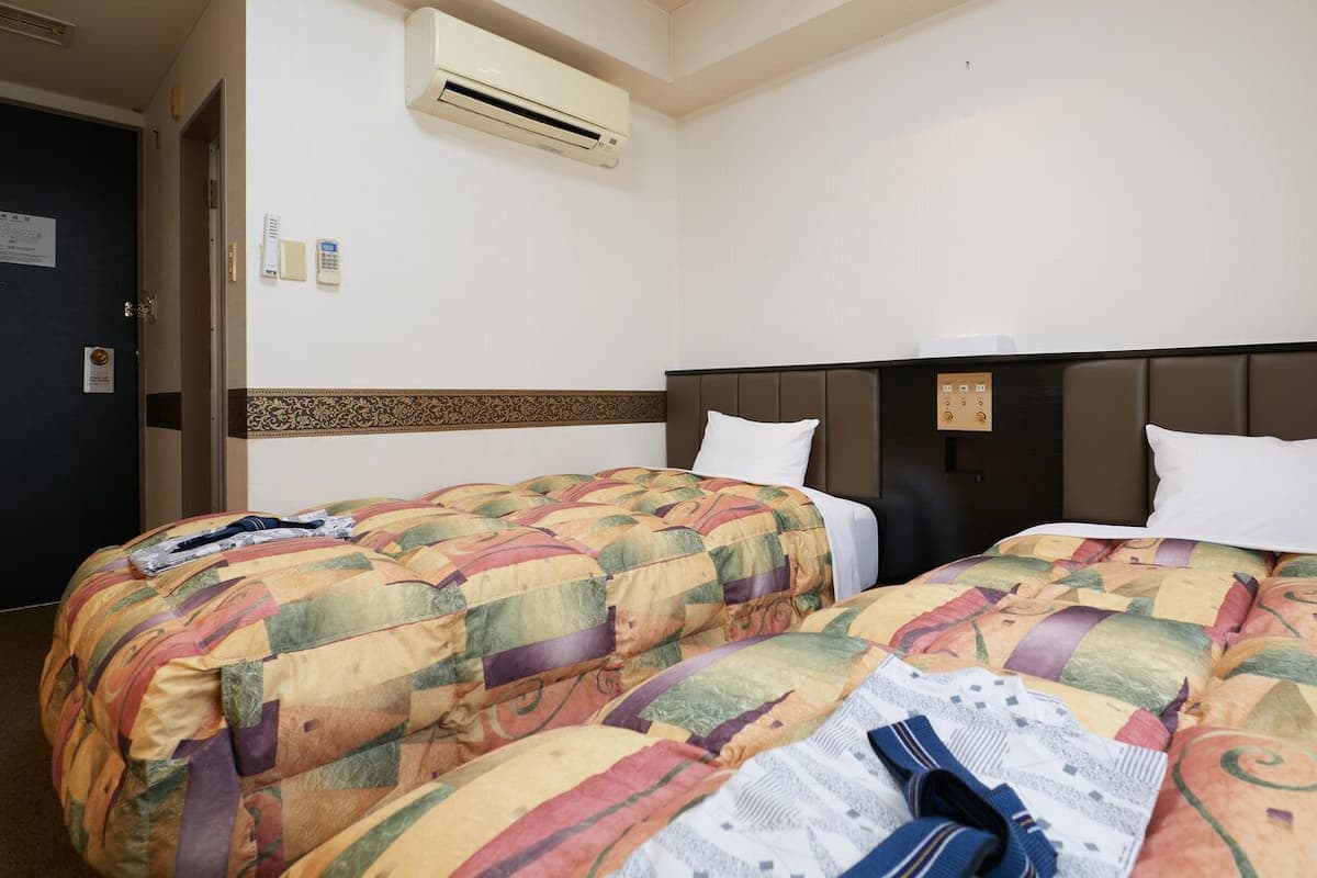 A hotel room with two beds, an air conditioning unit, a door, and a wall-mounted phone.