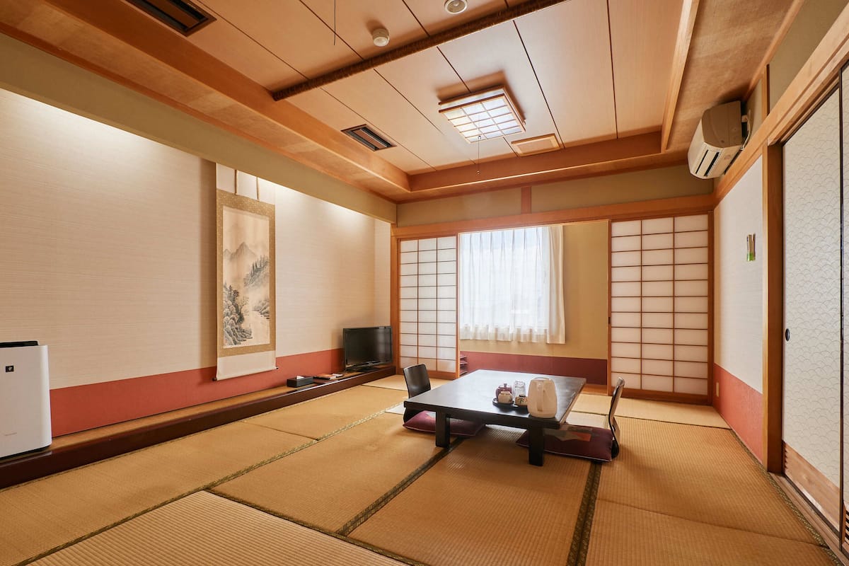 A traditional Japanese room with tatami flooring, a low table with cushions, a television, and a sliding door.