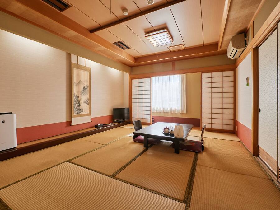 A traditional Japanese room with tatami flooring, a low table with cushions, a television, and a sliding door.