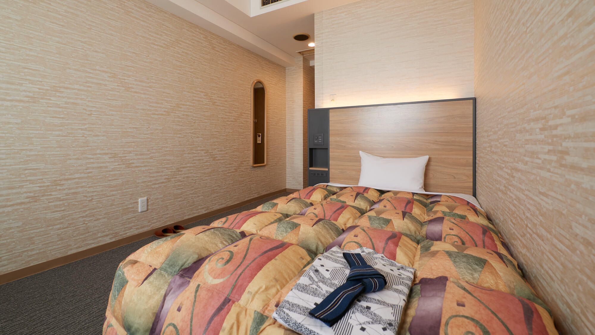 A hotel room with a bed, a headboard, a mirror, and a wall-mounted control panel.