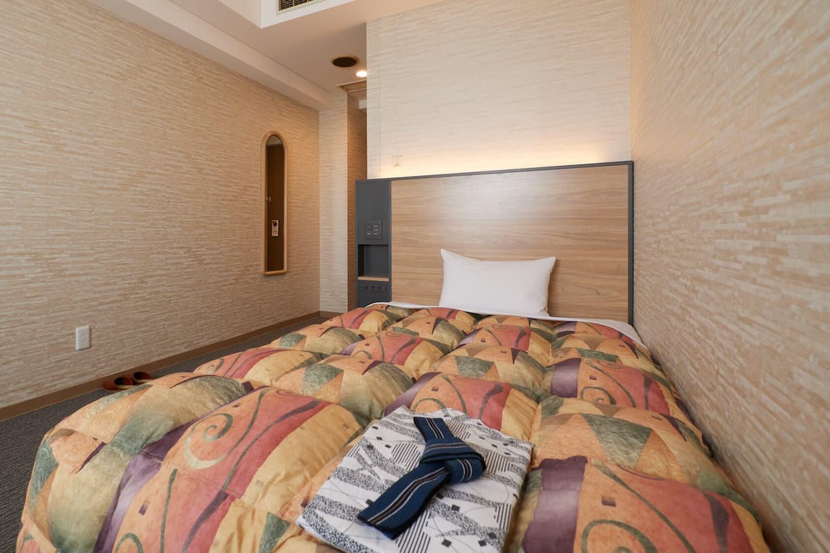 A hotel room with a bed, a headboard, a mirror, and a wall-mounted control panel.