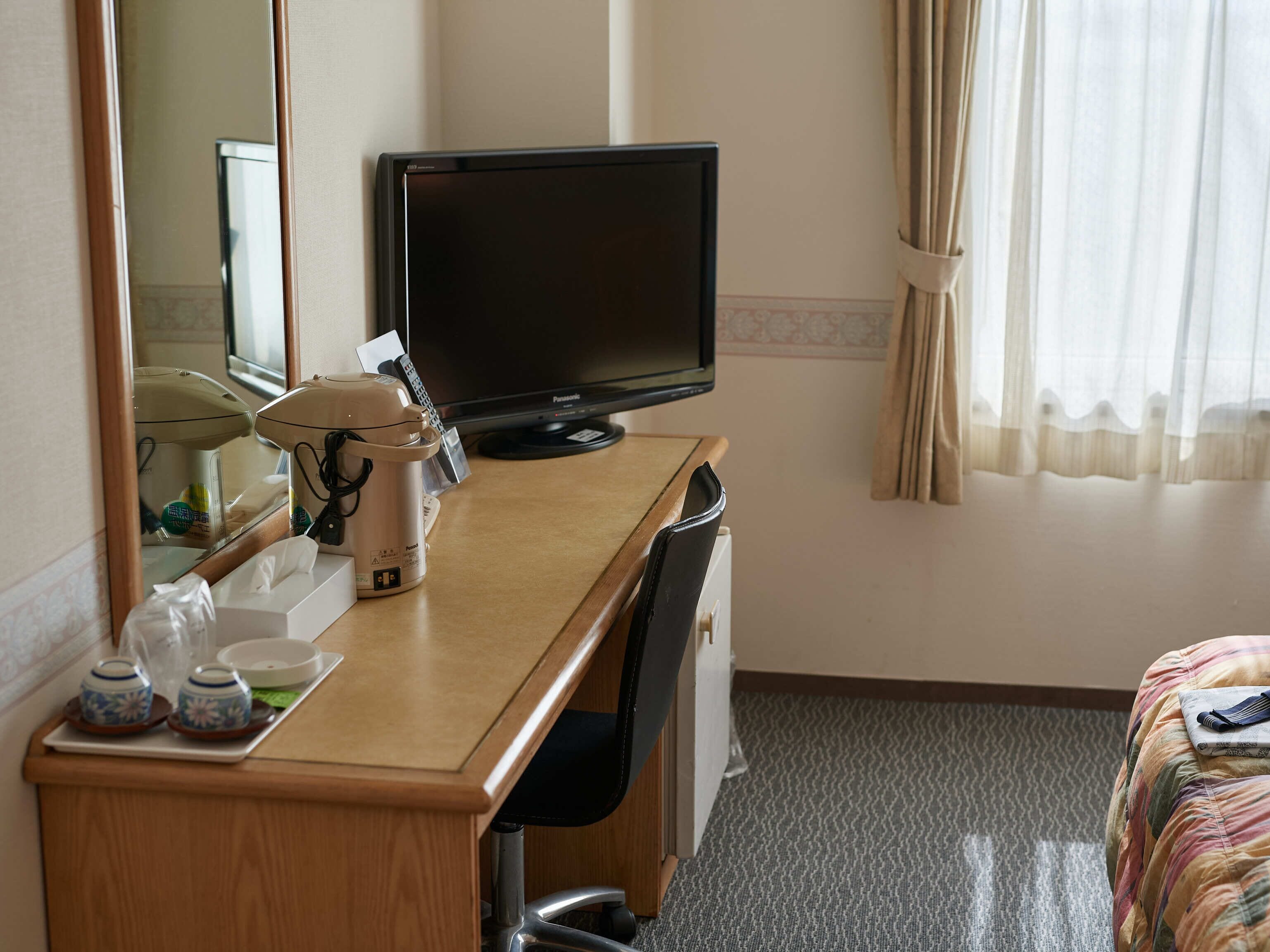 Habitación de hotel con escritorio de madera, televisión, cafetera y cama con manta a rayas.