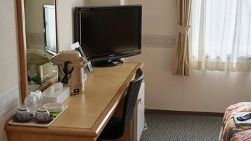 Habitación de hotel con escritorio de madera, televisión, cafetera y cama con manta a rayas.