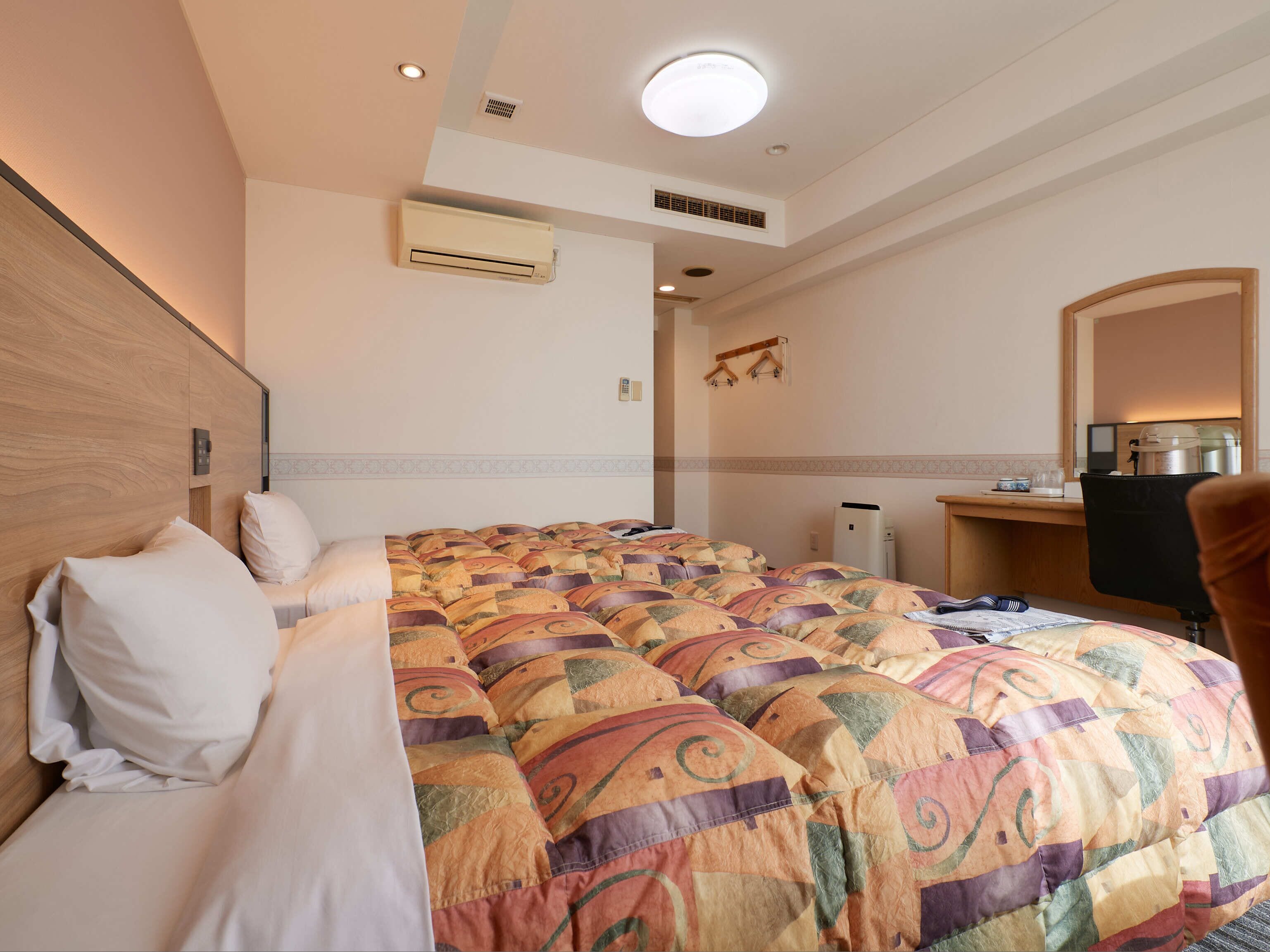 Una habitación de hotel con una cama grande, un equipo de aire acondicionado, un escritorio con una silla y un espejo.