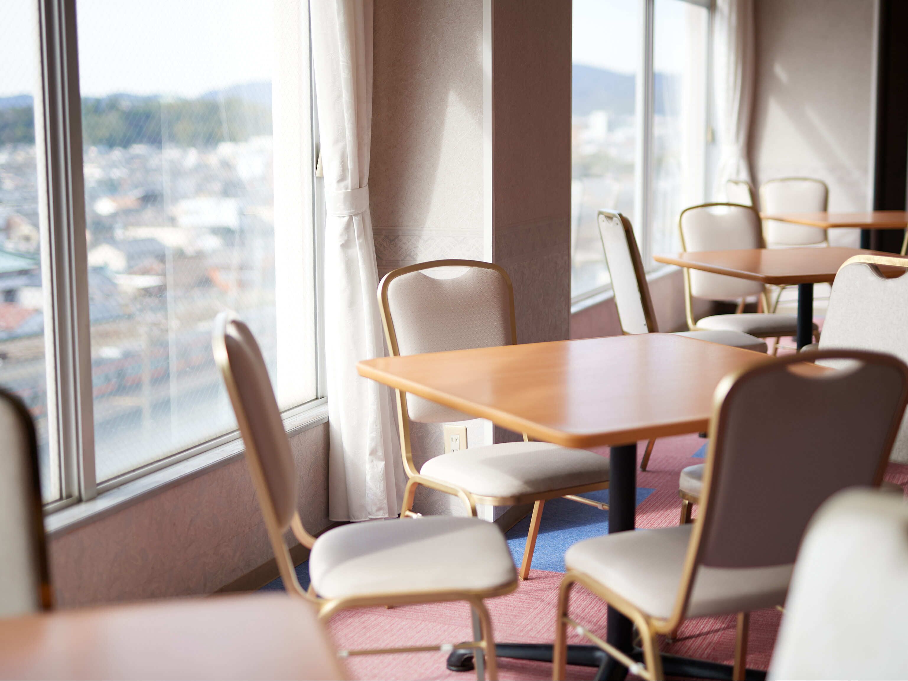 A conference room with tables and chairs, large windows with a city view, and a carpeted floor.