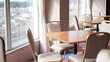 A conference room with tables and chairs, large windows with a city view, and a carpeted floor.