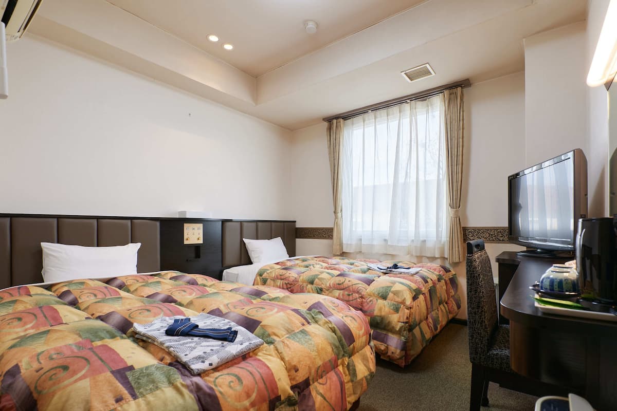 A hotel room with two beds, a television, and a desk with a coffee maker.