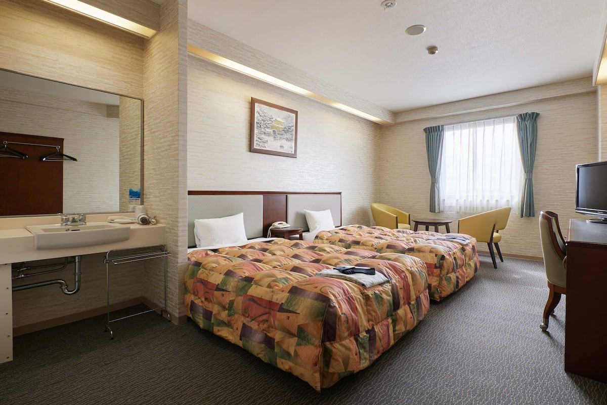 A hotel room with a large bed, a desk, a chair, a television, and a bathroom with a sink and mirror.