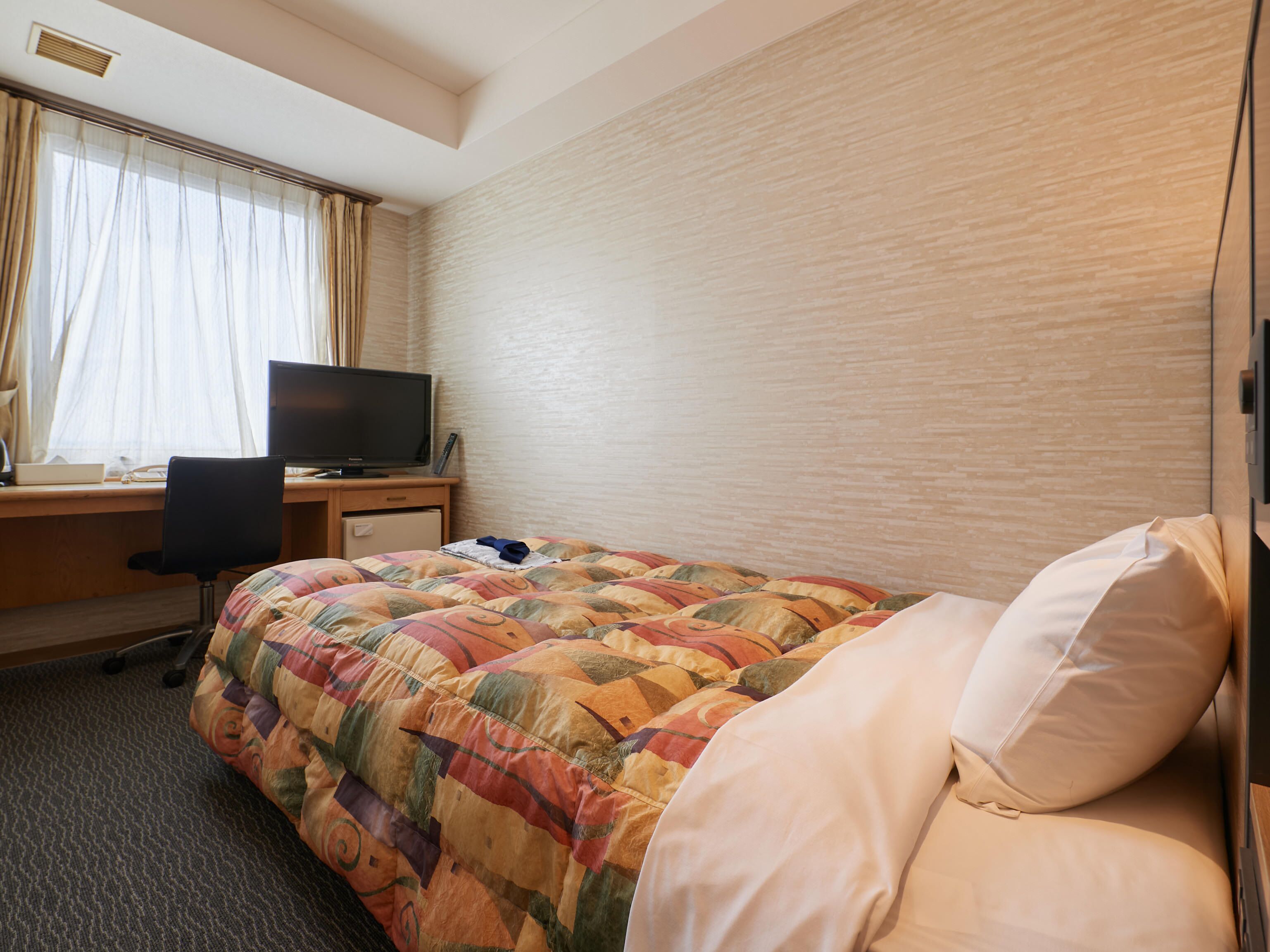 A hotel room with a bed, a desk with a computer, and a television.