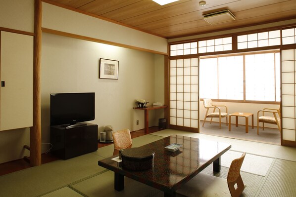 Una habitación tradicional japonesa con suelo de tatami, una mesa baja con cojines, un televisor y puertas correderas shoji.