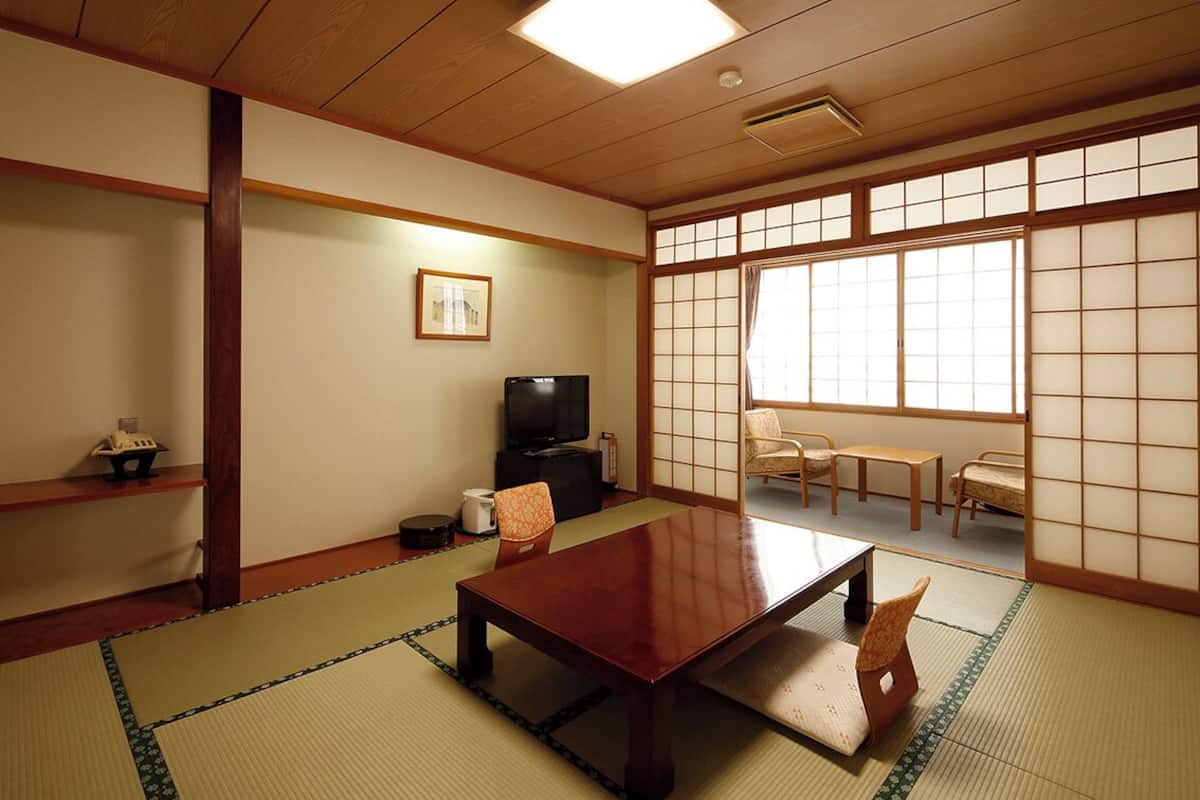 Une pièce de style japonais traditionnel, avec un sol recouvert de tatamis, une table basse, des chaises, un téléviseur et des portes coulissantes.