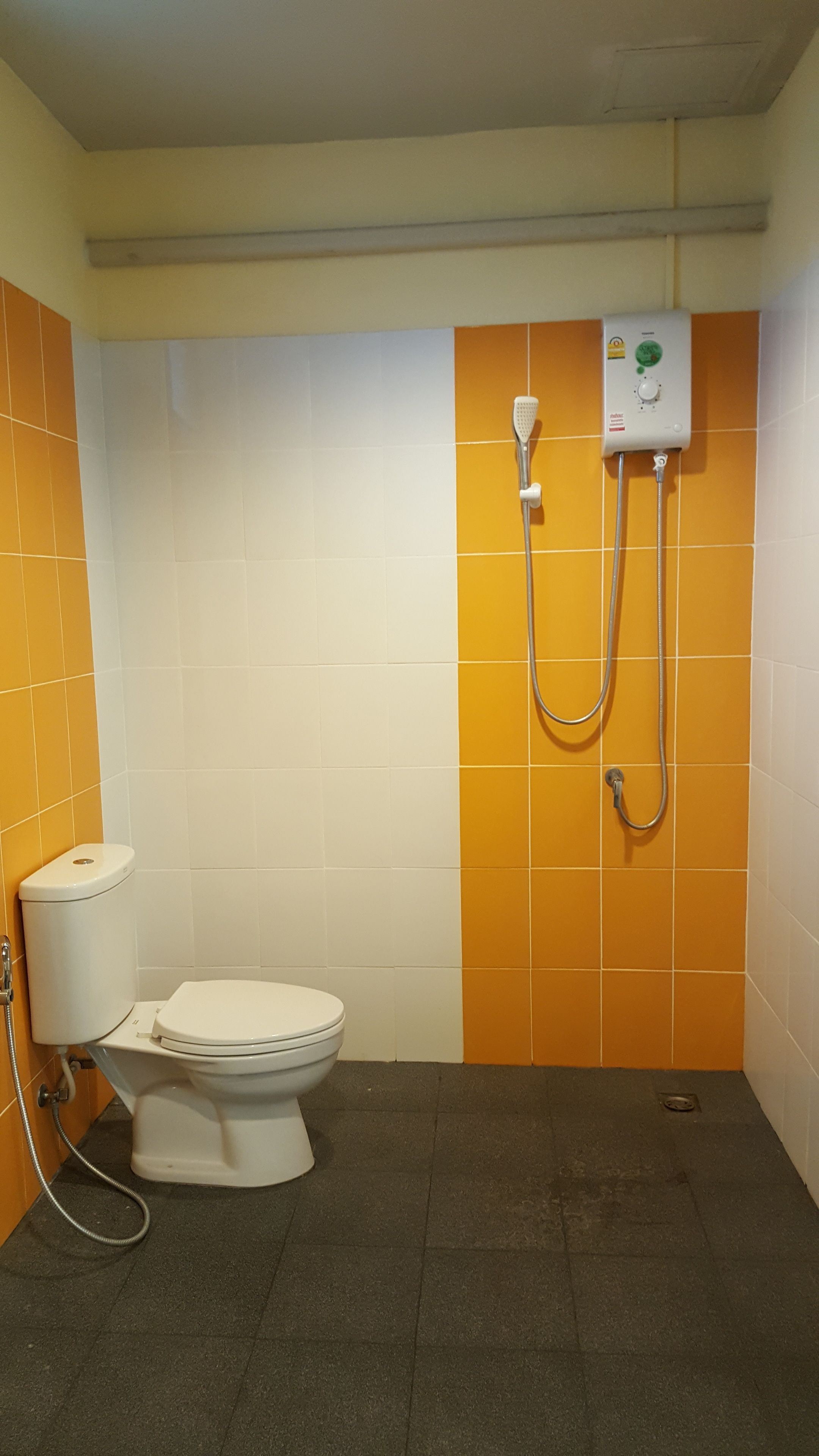Une petite salle de bain comprenant des toilettes, une douche et un panneau de commande fixé au mur.