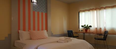 A hotel room with a bed, two chairs, a small table, a potted plant, and a window with curtains.