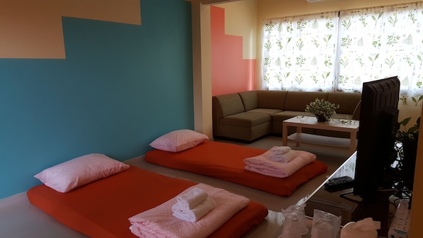 Una habitación con dos camas, un sofá, un televisor y una pequeña mesa con una planta.